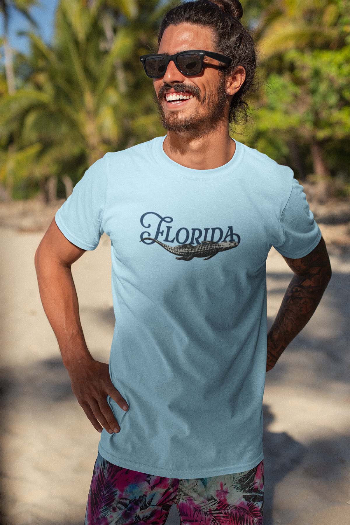 Man wearing a light blue 'Florida' t-shirt with sunglasses and floral shorts on a beach.